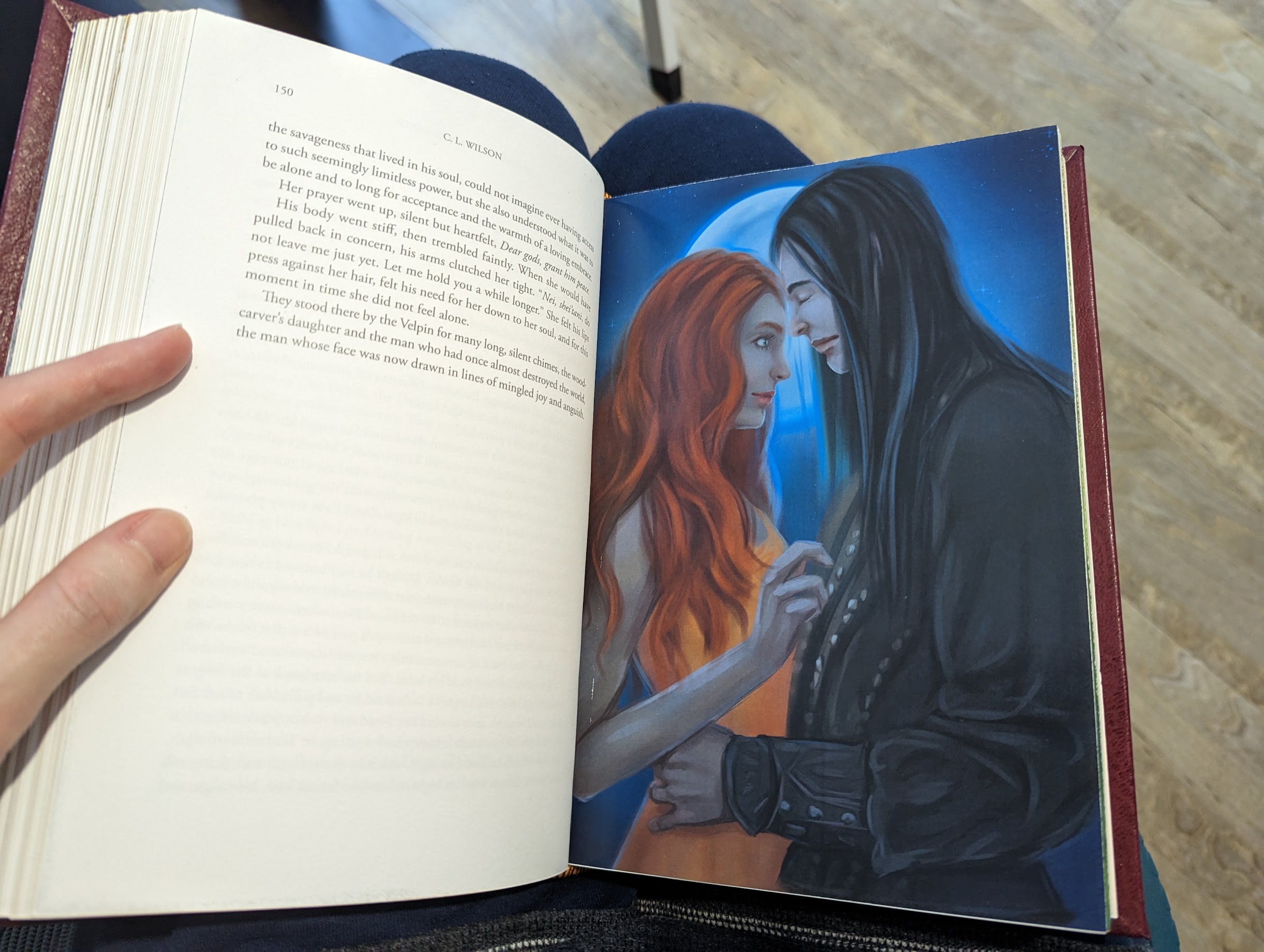 Photo of the inside page of a book. On the left-hand side is text from the book in black and white, and on the right-hand side is a full colour illustration. The illustration features a profile shot of a man and woman with their foreheads touching. The man's eyes are closed, and the woman is looking up at him a bit, shyly. In the background behind them is a full moon.
